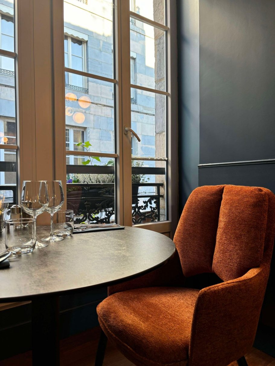 Fauteuil restaurant Besançon L'Y Gargotte Un coin de restaurant avec une table et une chaise orange, vue sur la rue à travers une fenêtre.