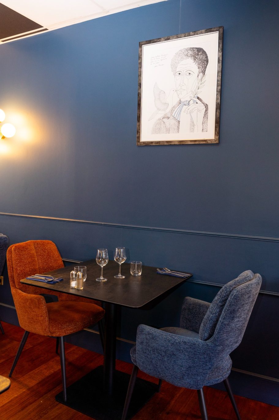 Décor 1er étage restaurant Besançon L'Y Gargotte Table avec chaises colorées dans un restaurant, mur bleu et tableau au-dessus.