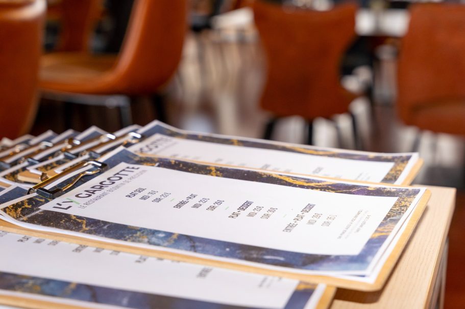 Menus à la semaine restaurant Besançon L'Y Gargotte Menus posés sur une table dans un restaurant, avec des chaises en arrière-plan.